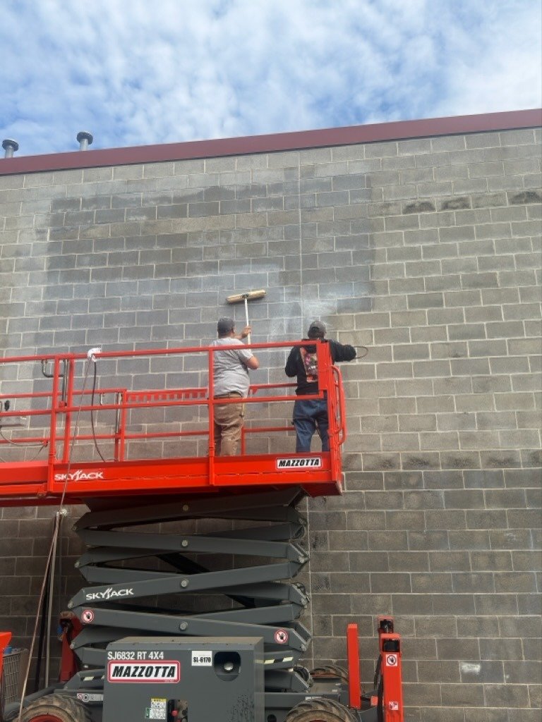 Two painters working from a scissor lift on a commercial block wall